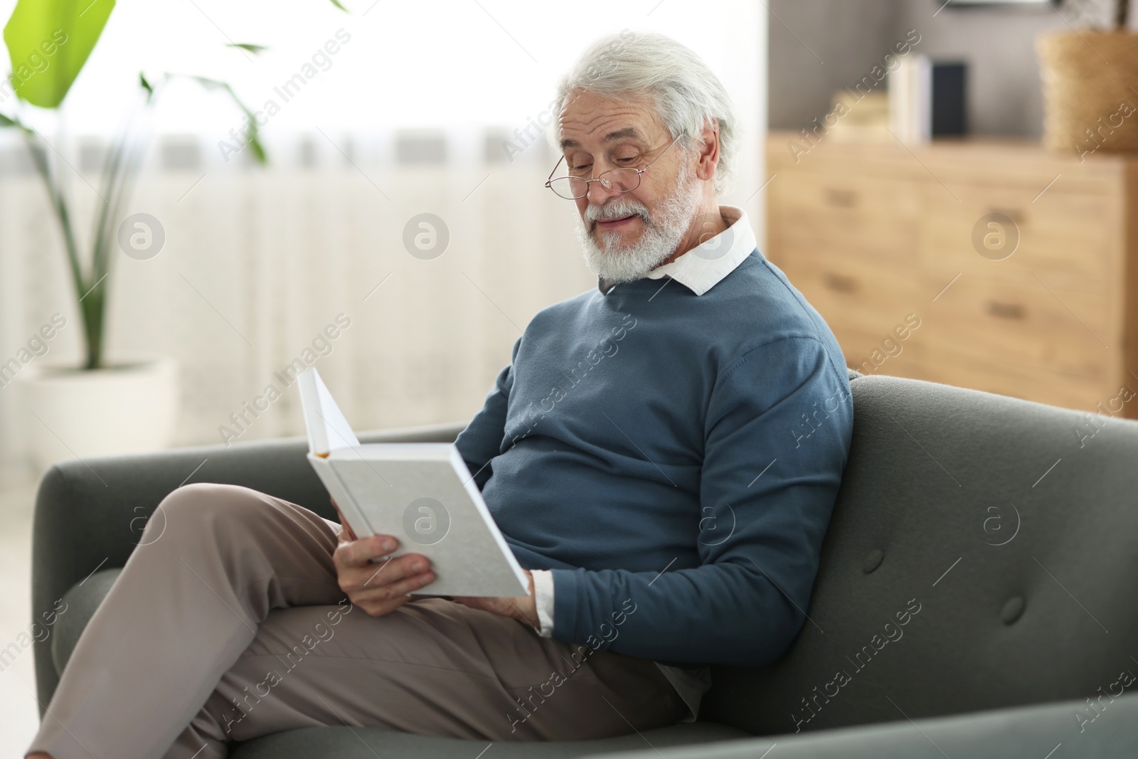 Photo of Portrait of happy grandpa reading book on sofa indoors