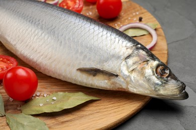 Photo of Tray with salted herring, onion, bay leaves and cherry tomatoes on black table, closeup