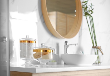 Photo of Jars with cotton pads and loofah sponges on countertop in bathroom