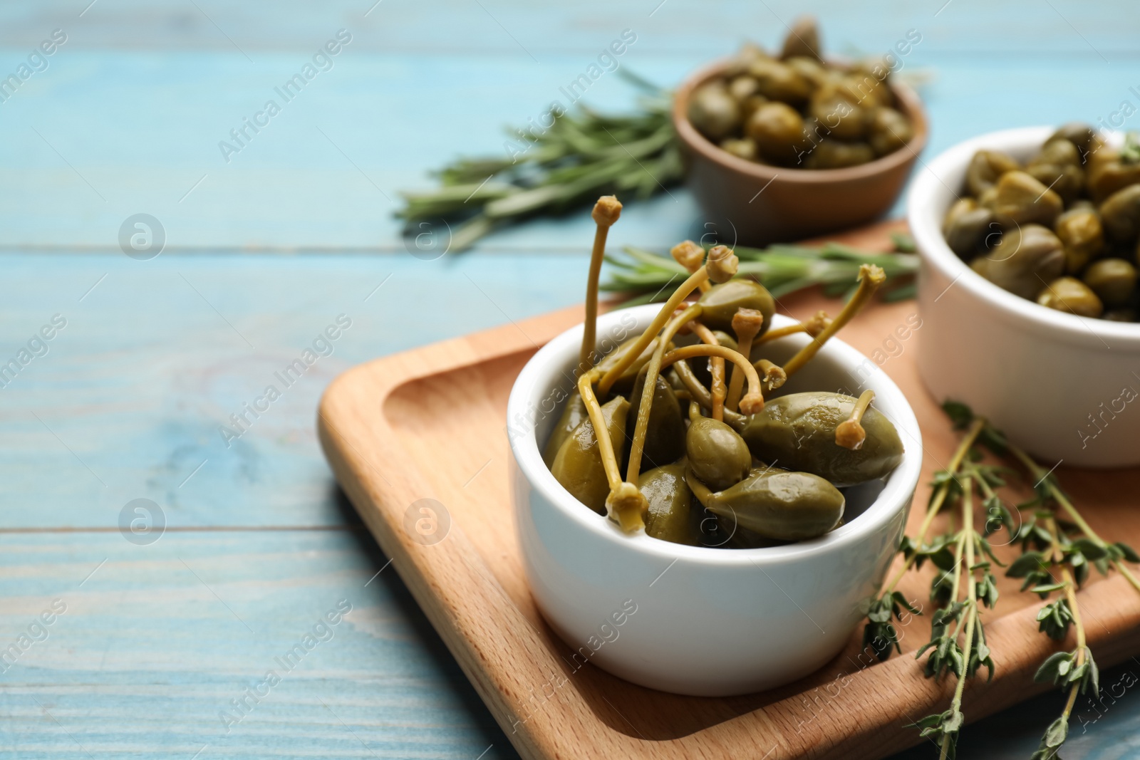 Photo of Tasty capers, thyme and rosemary on light blue wooden table, space for text