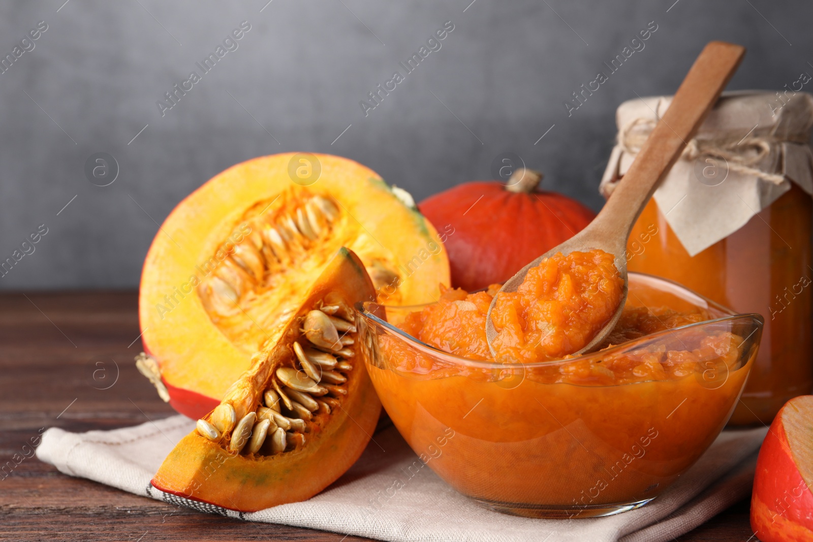 Photo of Bowl of pumpkin jam and fresh pumpkin on wooden table