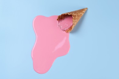 Photo of Melted ice cream and wafer cone on light blue background, above view