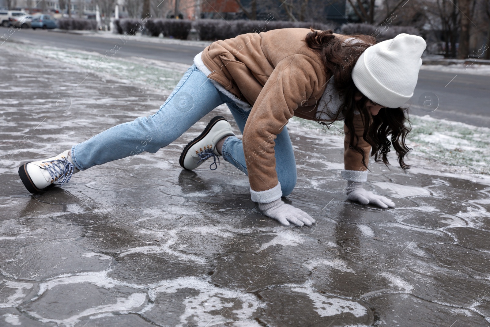 Photo of Young woman trying to stand up after falling on slippery icy pavement outdoors