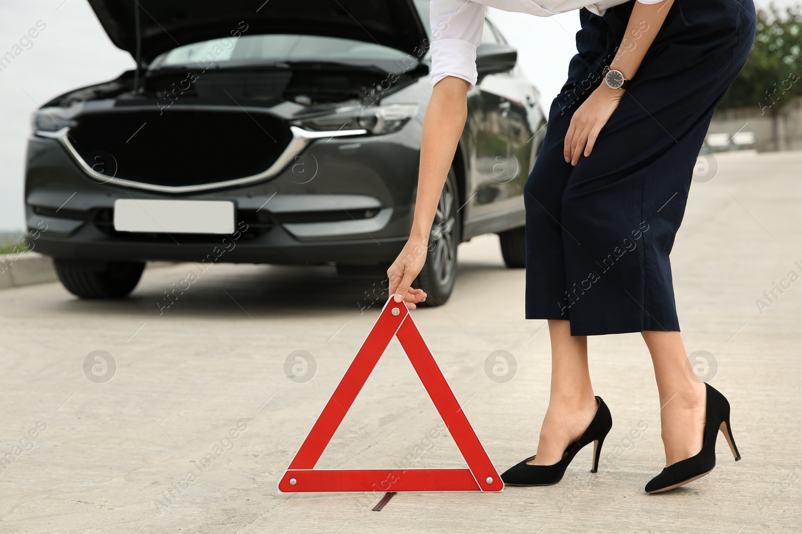 Photo of Woman putting emergency stop sign near broken car, closeup