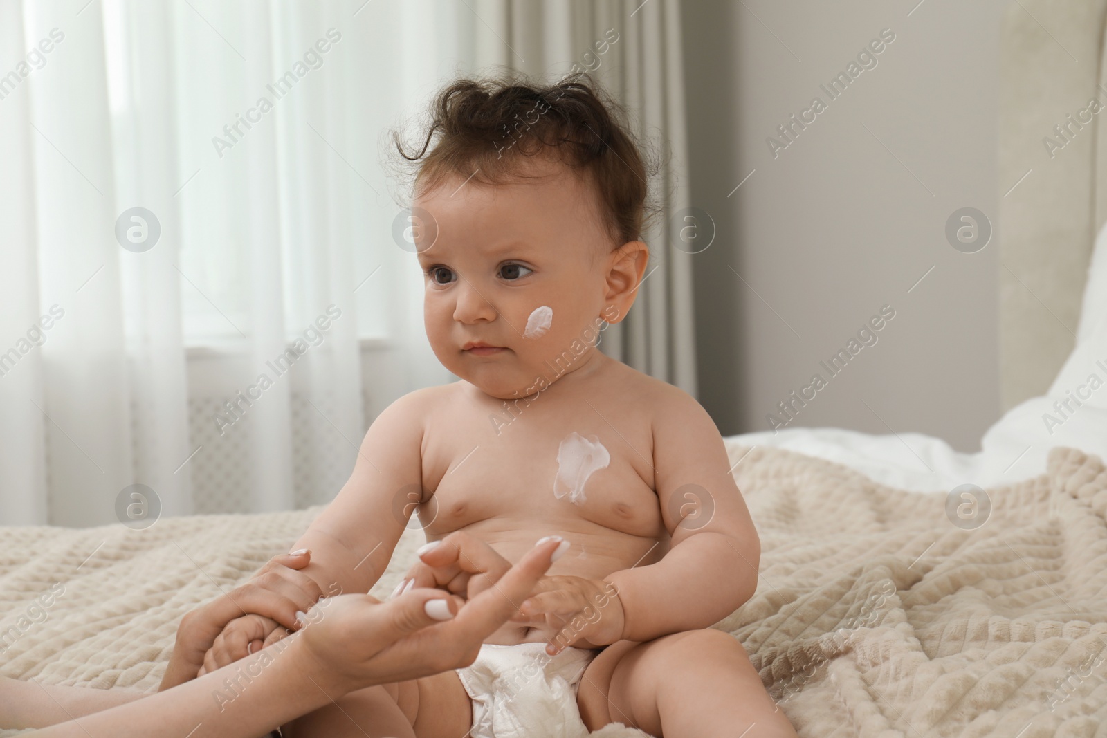 Photo of Mother applying body cream on her baby in bedroom