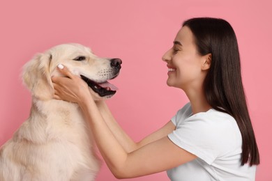 Happy woman playing with cute Labrador Retriever dog on pink background. Adorable pet