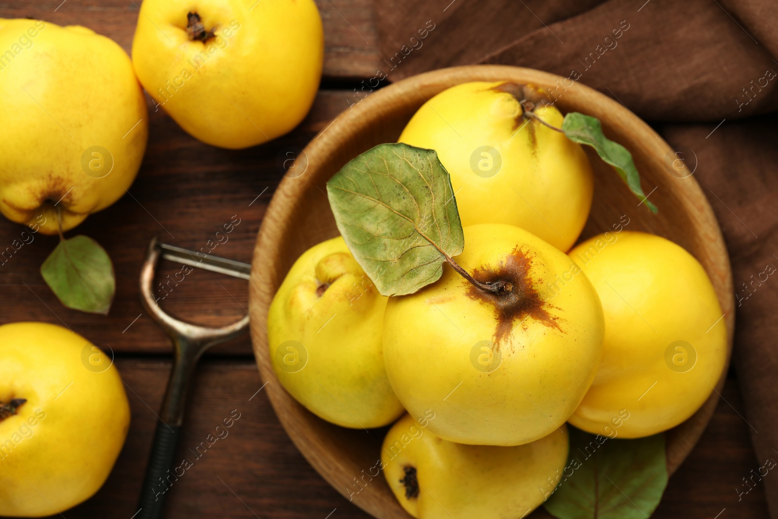 Photo of Tasty ripe quince fruits in bowl and peeler on wooden table, flat lay