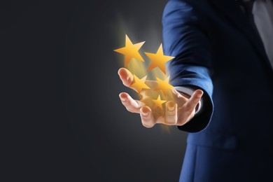 Image of Man holding virtual stars on black background, closeup. Customer satisfaction score