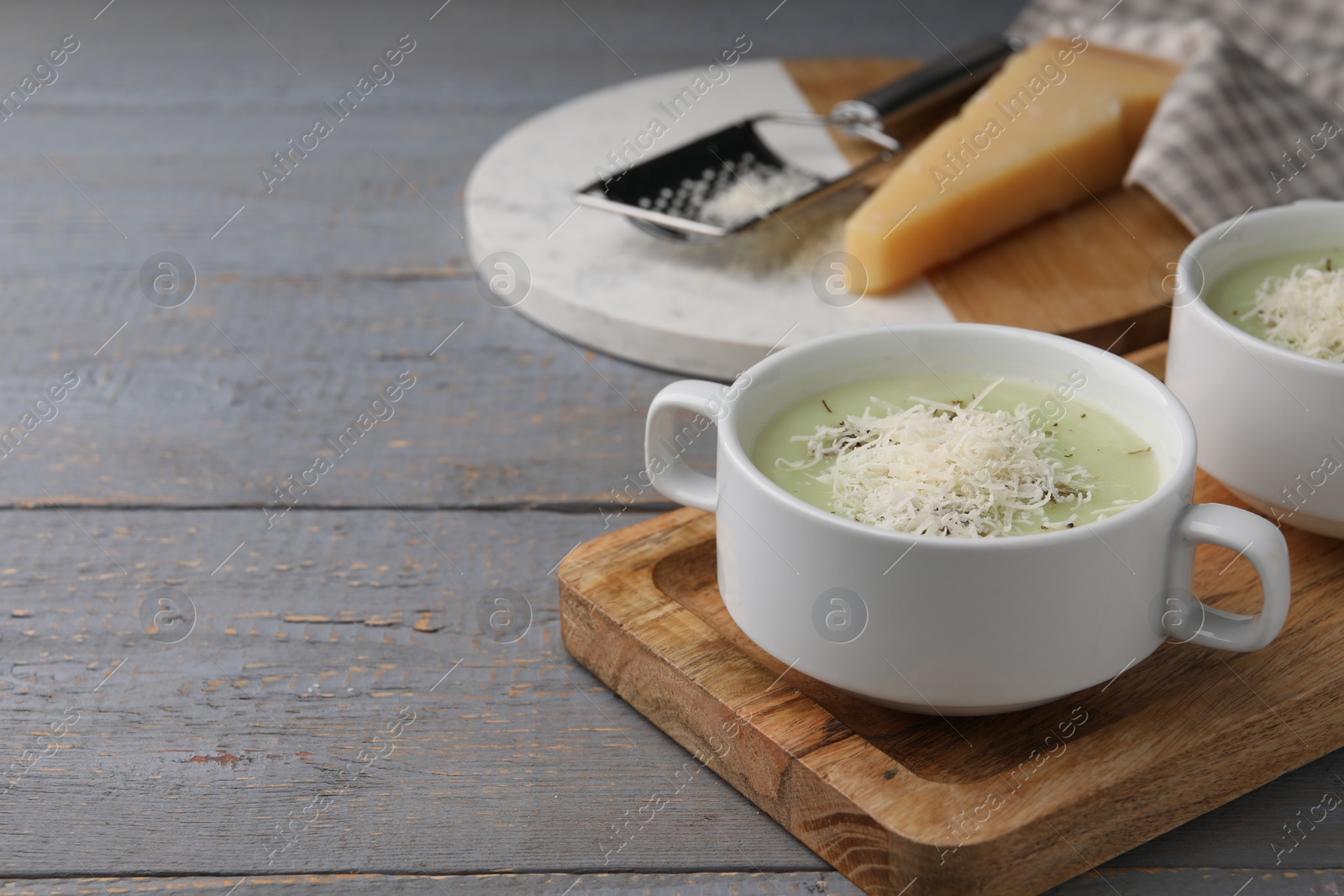 Photo of Delicious cream soup with parmesan cheese in bowls on grey wooden table. Space for text