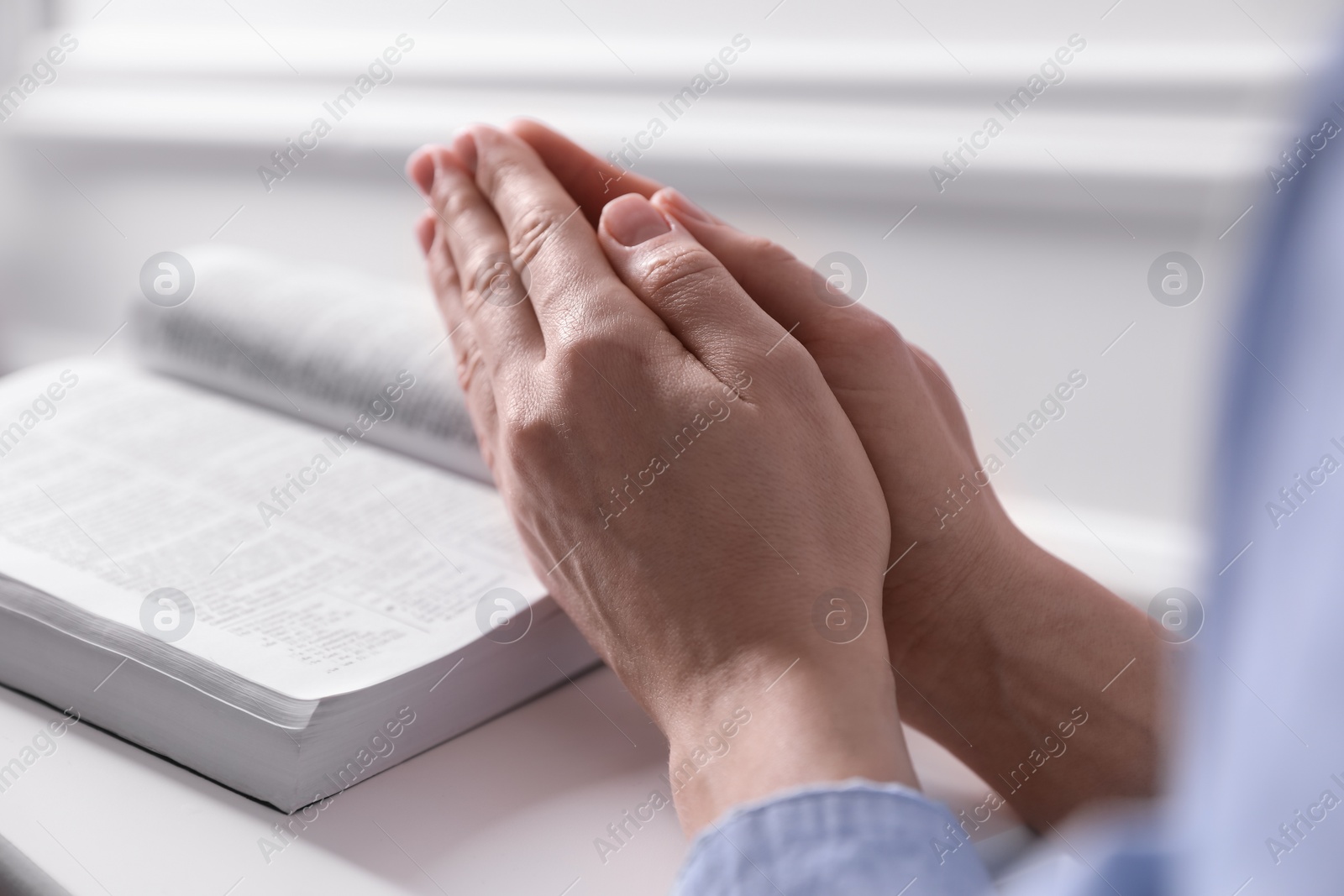 Photo of Religion. Christian woman praying over Bible indoors, closeup