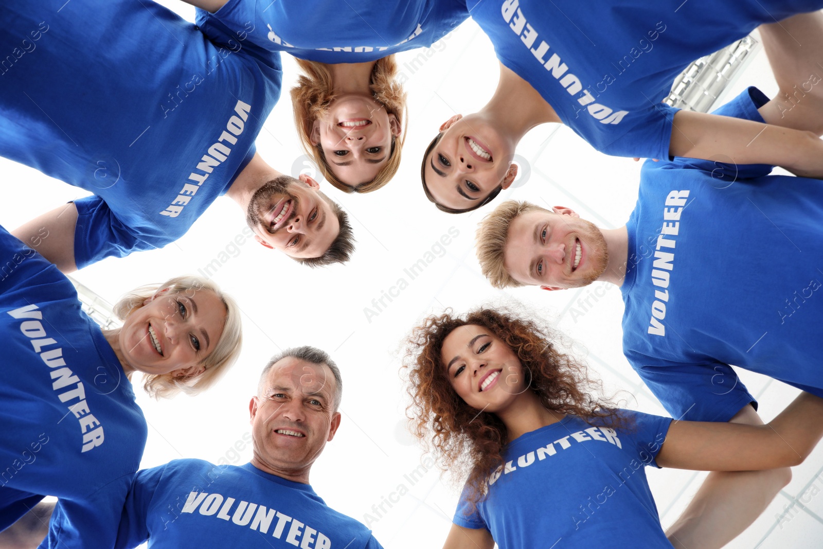 Photo of Team of volunteers joined in circle on light background, bottom view