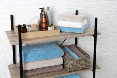 Shelving unit with clean towels and toiletries near brick wall