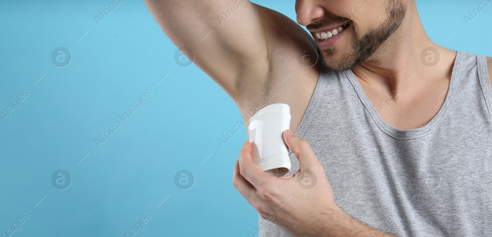 Photo of Man applying deodorant on turquoise background, closeup. Space for text