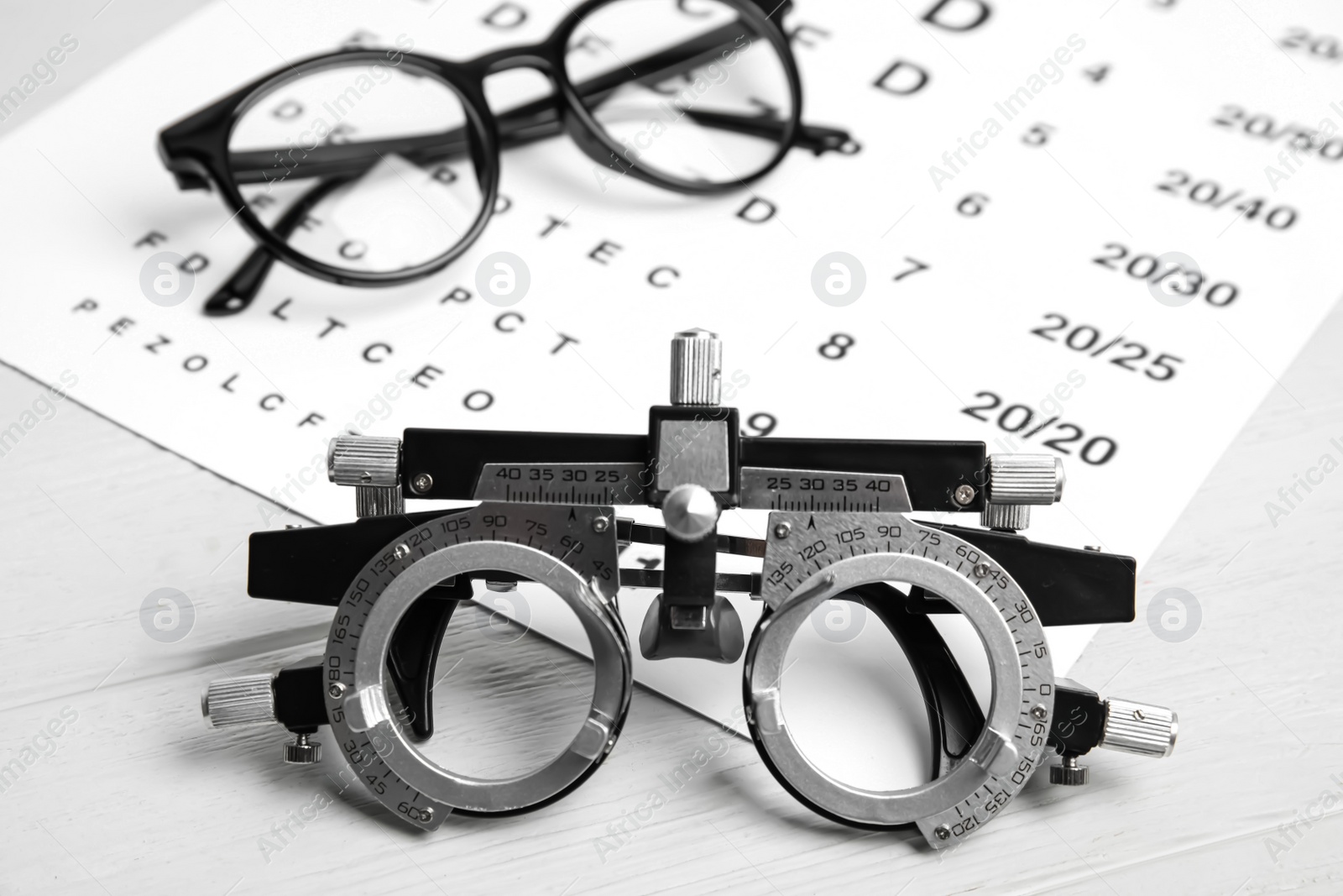 Photo of Trial frame, eye chart test and glasses on white wooden table. Ophthalmologist tools