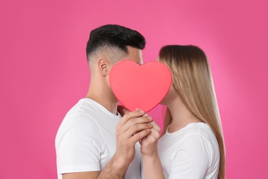 Photo of Lovely couple kissing behind decorative heart on pink background. Valentine's day celebration