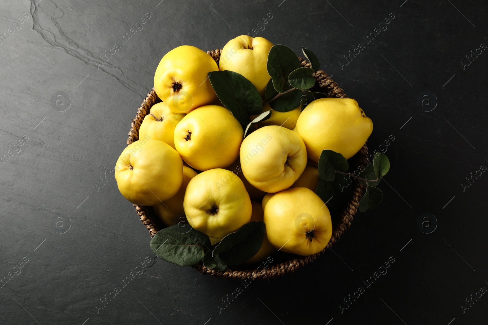 Photo of Fresh ripe organic quinces with leaves in wicker basket on black table, top view