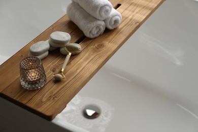 Photo of Wooden tray with spa products and burning candle on bath tub