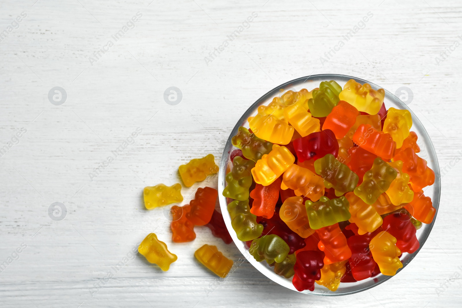 Photo of Bowl with delicious bright jelly bears on white wooden table, top view. Space for text