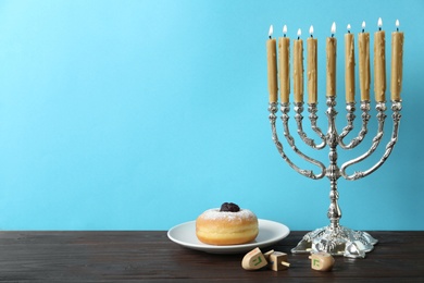 Silver menorah, dreidels with He, Pe, Nun, Gimel letters and sufganiyah on wooden table, space for text. Hanukkah symbols