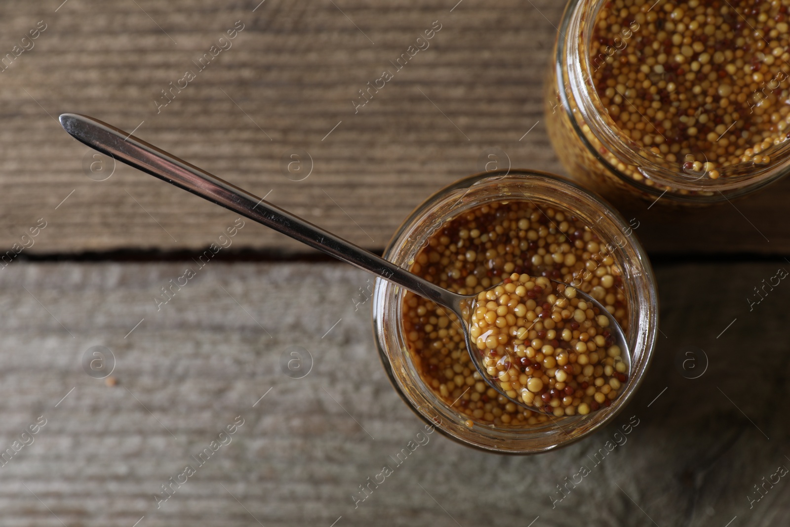 Photo of Jars and spoon of whole grain mustard on wooden table, flat lay. Space for text