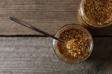 Photo of Jars and spoon of whole grain mustard on wooden table, flat lay. Space for text