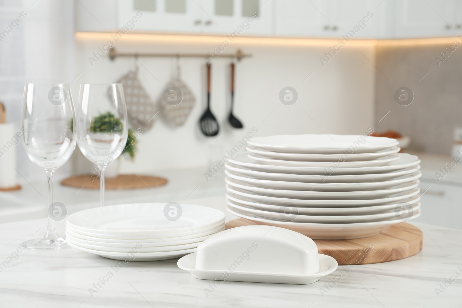 Photo of Clean plates, glasses and butter dish on white marble table in kitchen