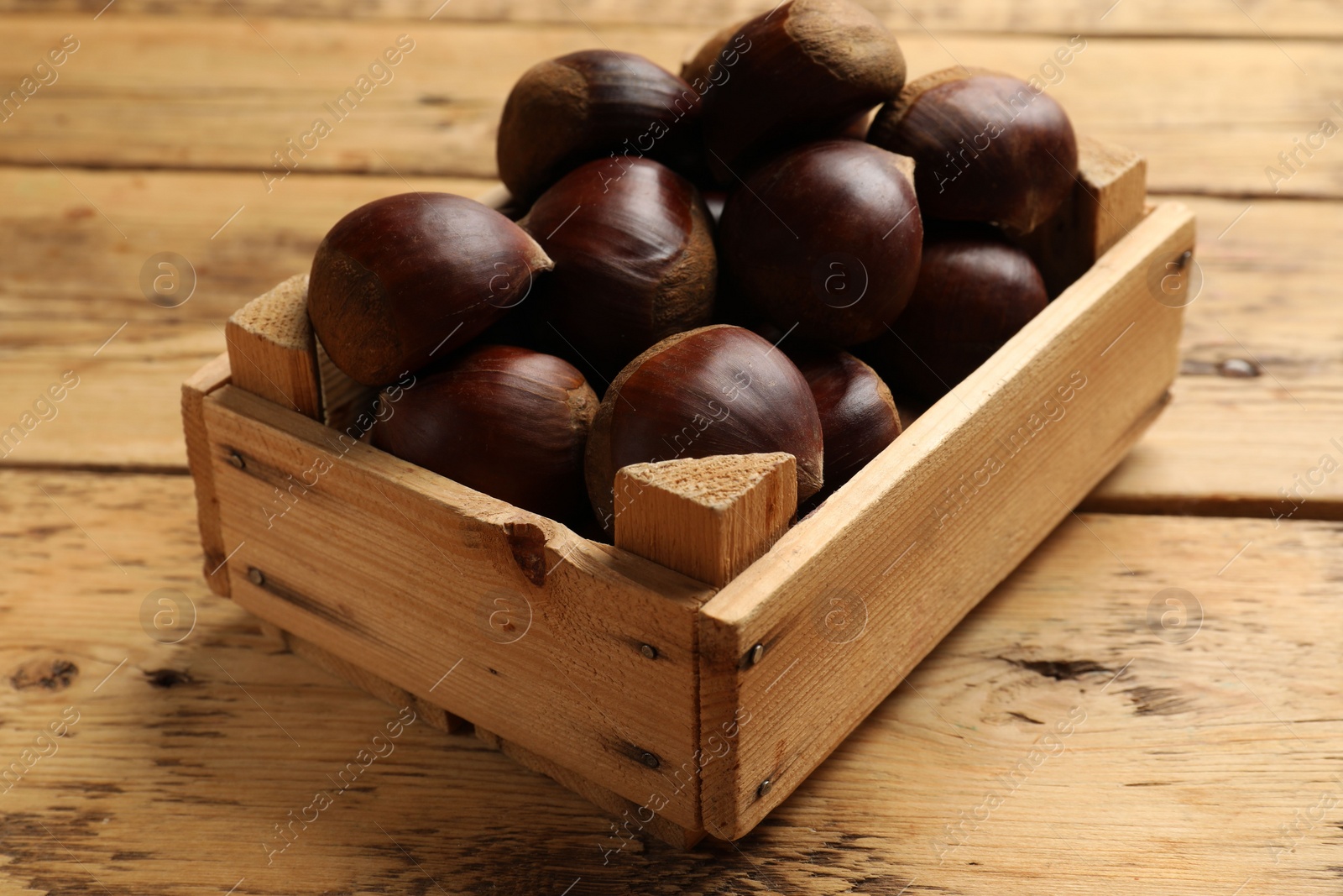 Photo of Sweet fresh edible chestnuts in crate on wooden table