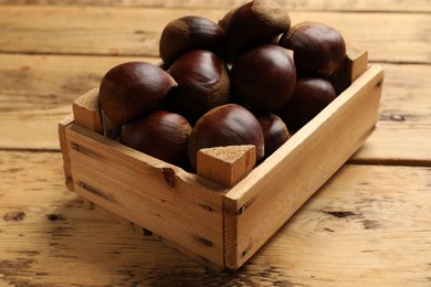 Photo of Sweet fresh edible chestnuts in crate on wooden table