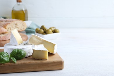 Photo of Tasty brie cheese with basil on white wooden table, space for text