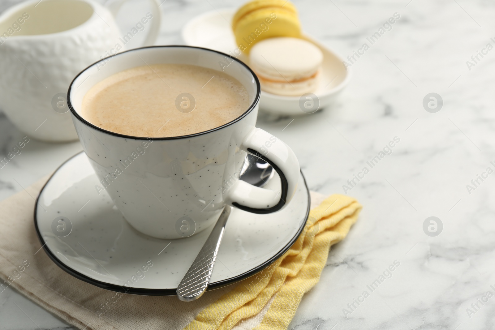 Photo of Tasty cappuccino in cup, spoon and saucer on white marble table, closeup. Space for text