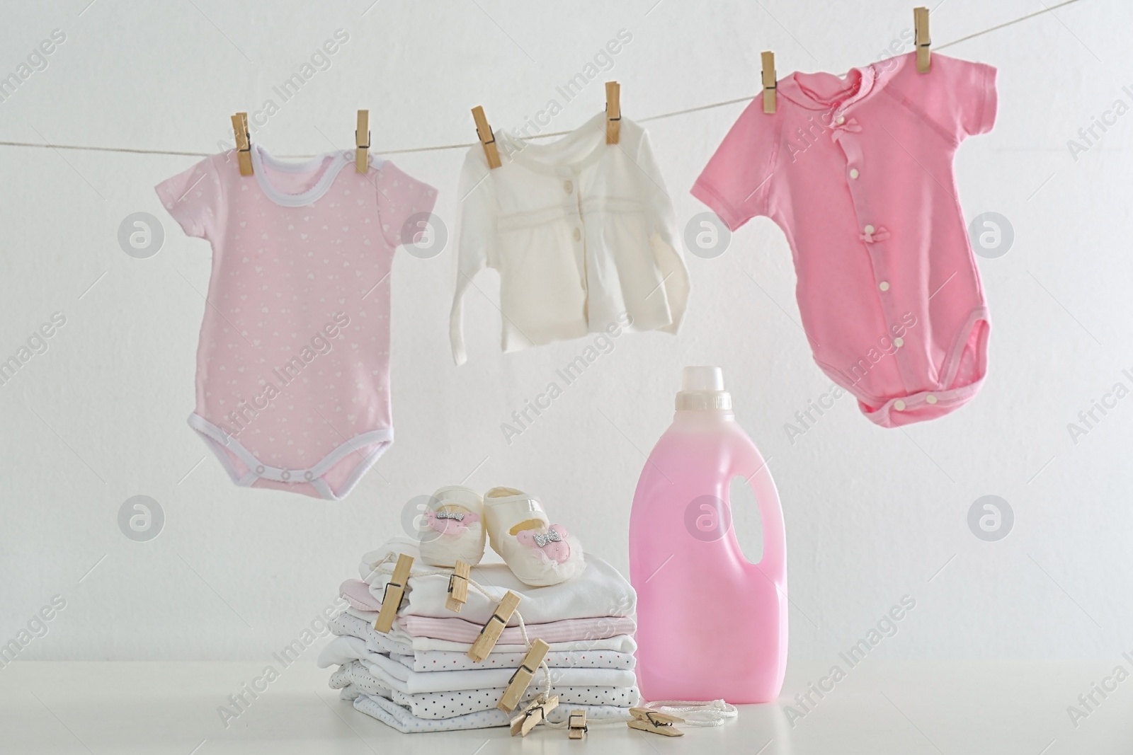 Photo of Fresh baby laundry hanging on clothesline and bottle of detergent on white background