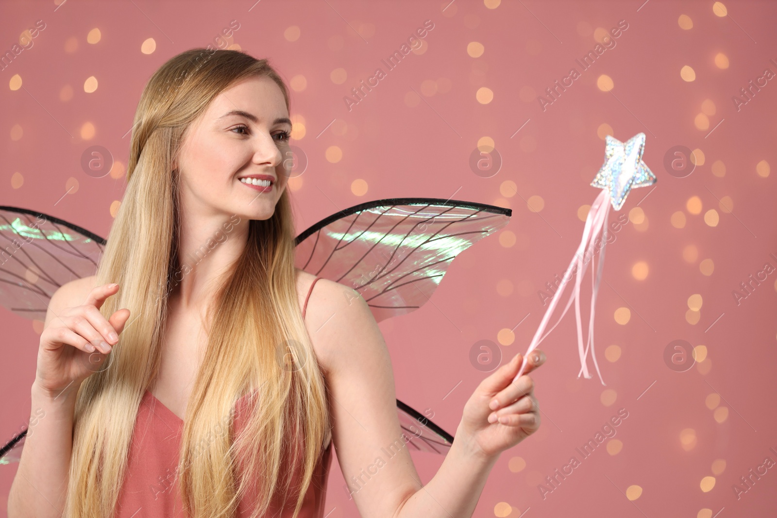 Photo of Beautiful girl in fairy costume with wings and magic wand on pink background