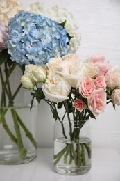 Photo of Beautiful hydrangea and rose flowers in vases on white table, closeup