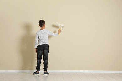 Photo of Child painting color wall with roller brush. Space for text