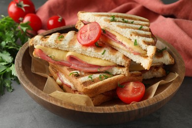 Tasty sandwiches with ham, tomato and melted cheese in bowl on grey table, closeup