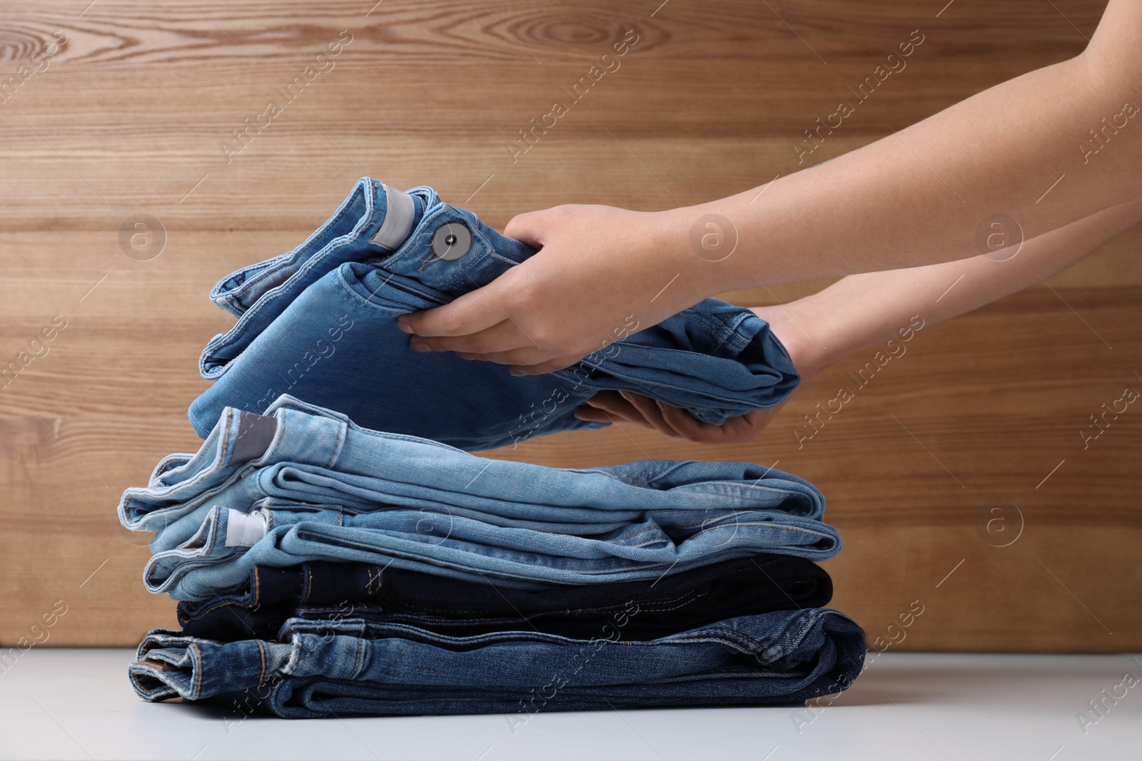 Photo of Young woman folding stylish jeans on table