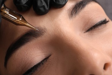 Young woman undergoing procedure of permanent eyebrow makeup in tattoo salon, closeup