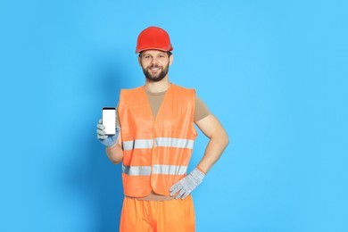 Man in reflective uniform showing smartphone on light blue background