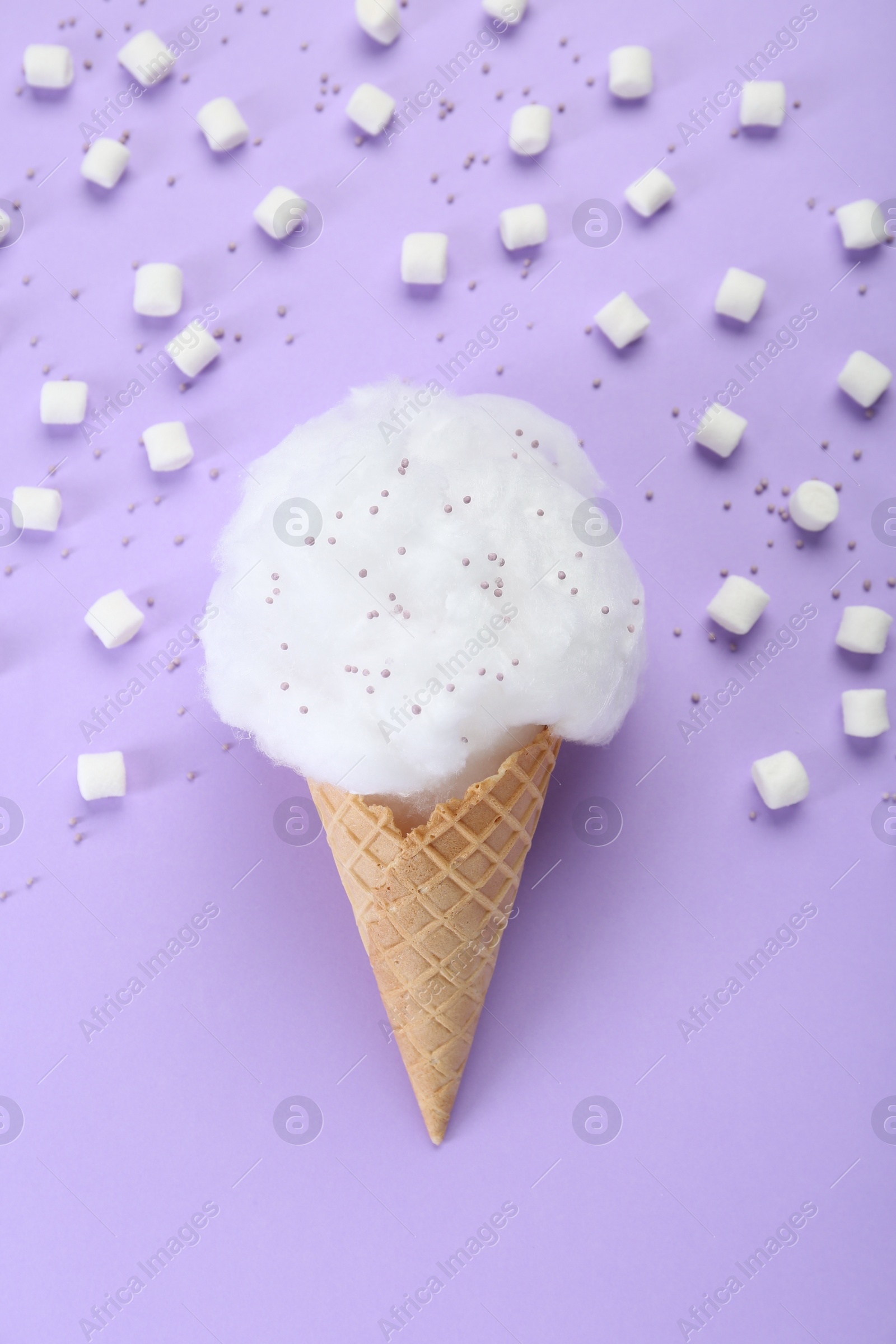 Photo of Sweet cotton candy in waffle cone and marshmallows on purple background, flat lay