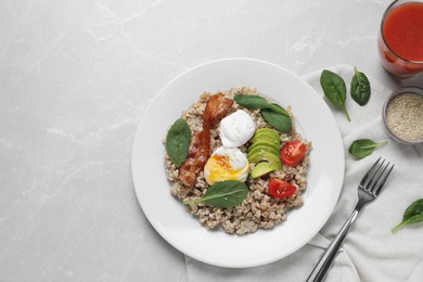 Delicious boiled oatmeal with poached egg, bacon, avocado and tomato served on light grey marble table, flat lay. Space for text