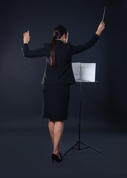 Photo of Professional conductor with baton and note stand on dark background, back view