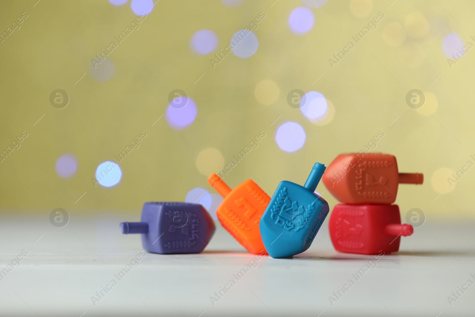 Photo of Hanukkah celebration. Dreidels with jewish letters against pale yellow background with blurred lights, closeup