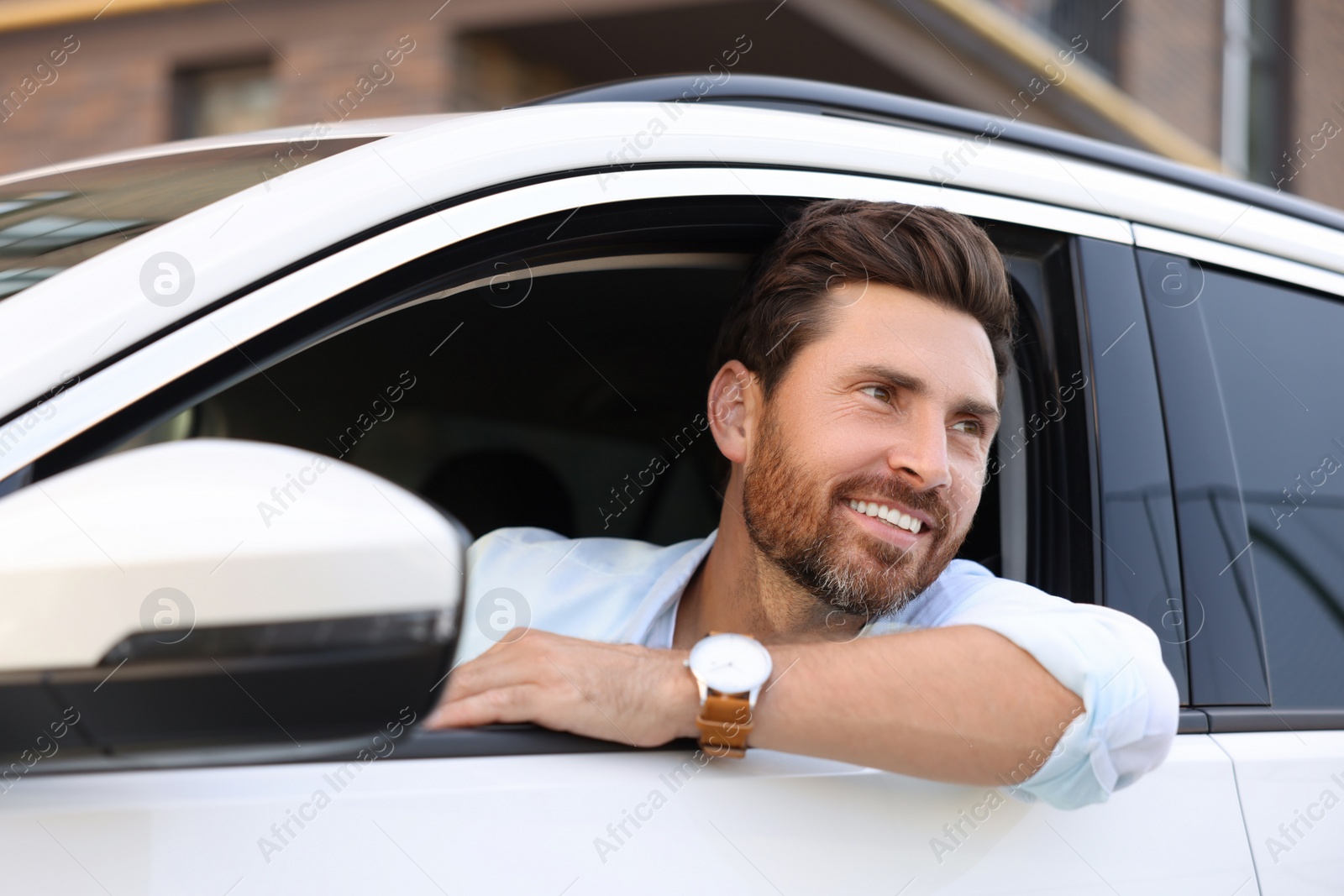 Photo of Happy bearded man looking out of car window on city street, view from outside. Enjoying trip