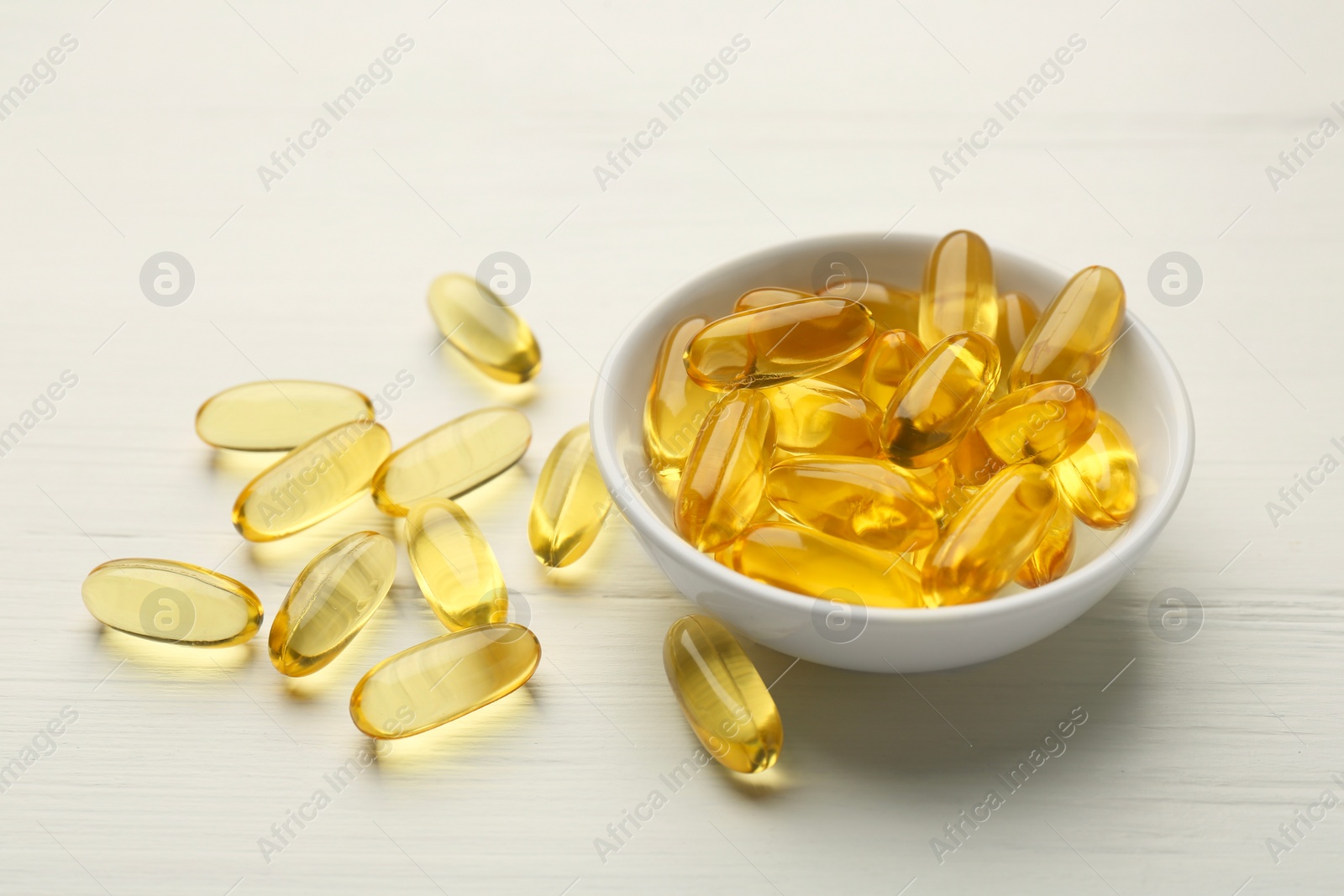 Photo of Vitamin capsules in bowl on white wooden table