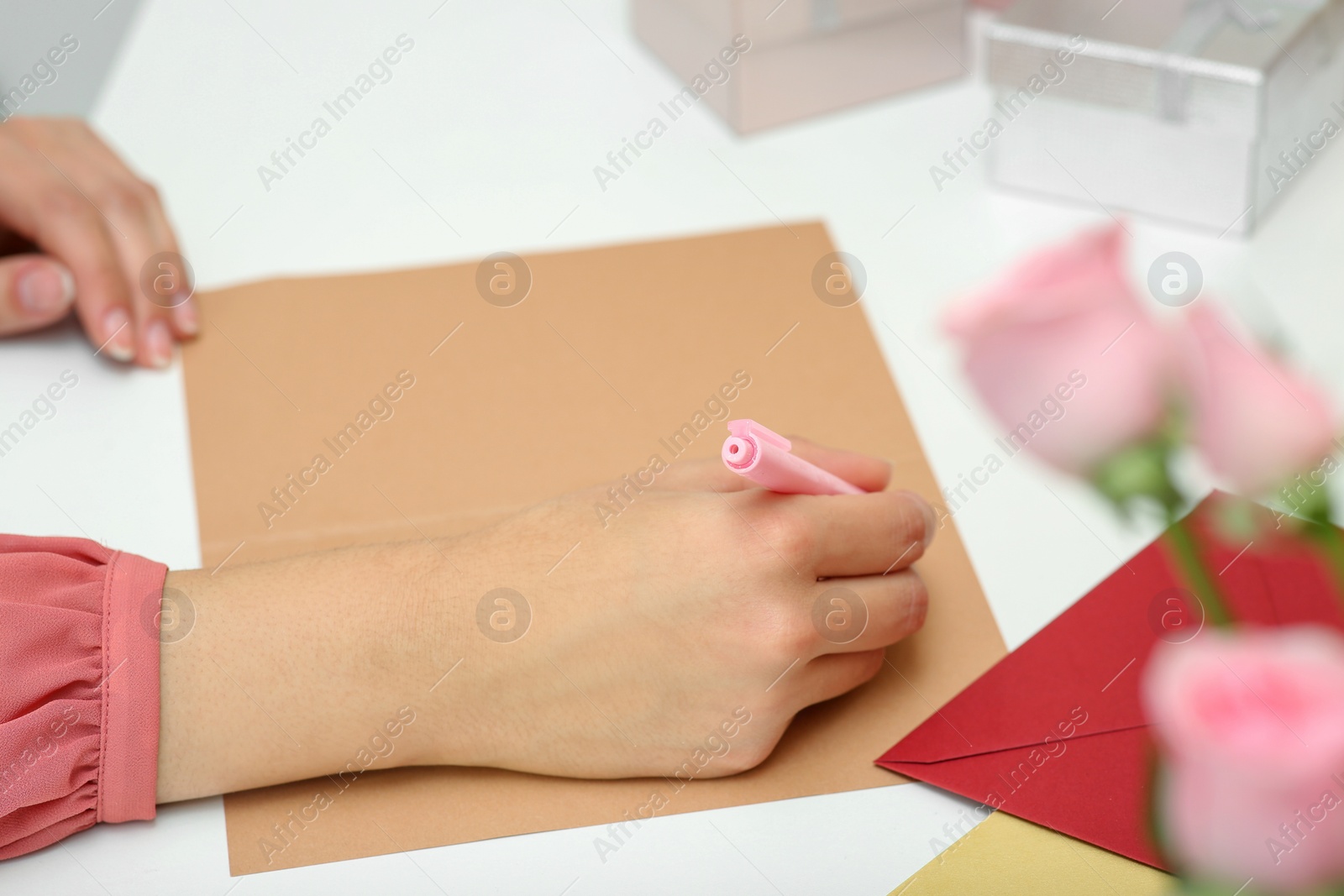 Photo of Young woman writing message in greeting card at white table, closeup