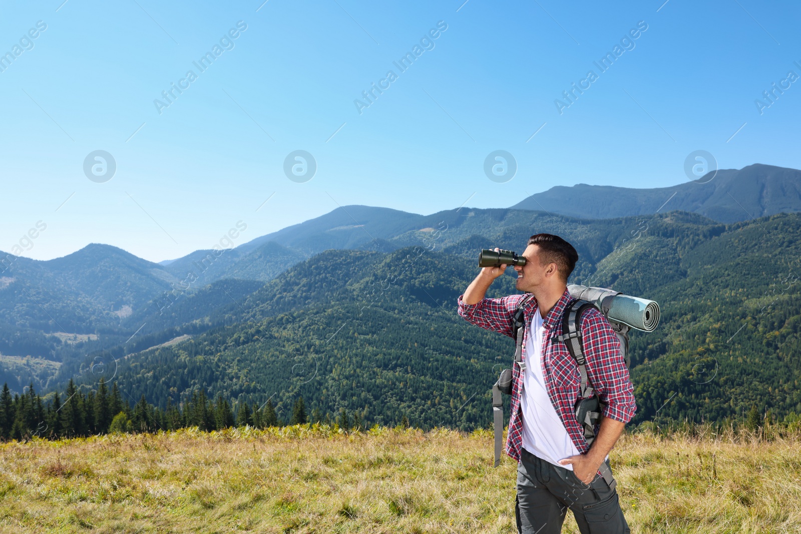 Photo of Tourist with hiking equipment looking through binoculars in mountains