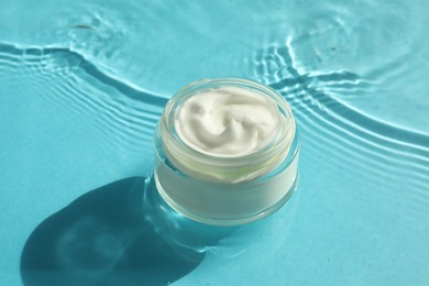 Photo of Jar with moisturizing cream in water on light blue background