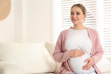 Photo of Young pregnant woman on sofa at home. Space for text