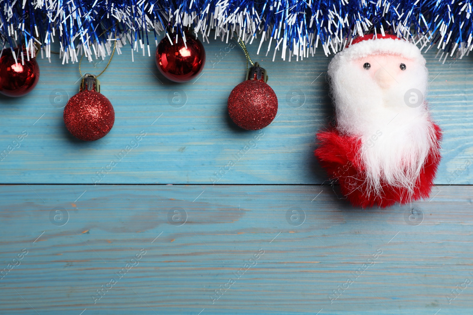 Photo of Bright tinsel, toy Santa and Christmas balls on light blue wooden background, flat lay. Space for text