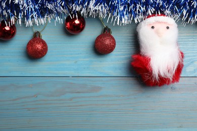 Bright tinsel, toy Santa and Christmas balls on light blue wooden background, flat lay. Space for text